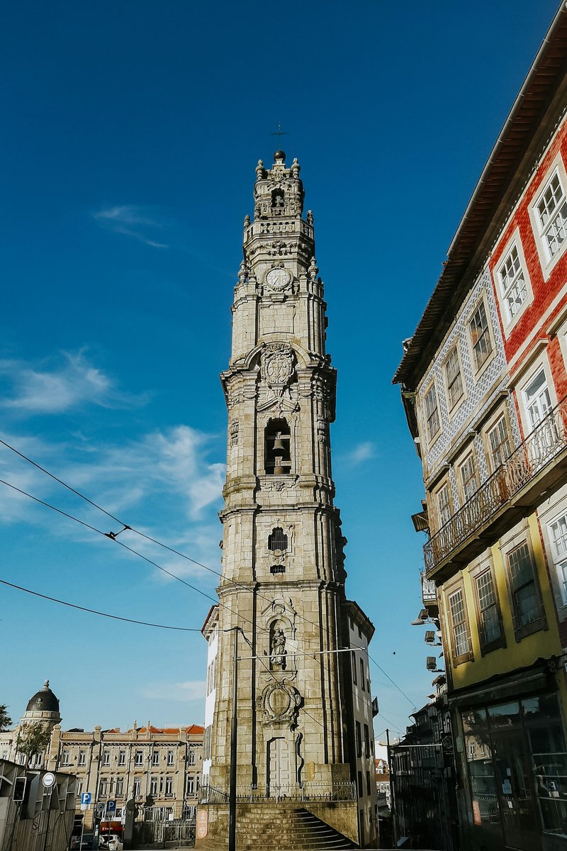 The granite Baroque bell tower of Torre dos Clérigos rising above the terracotta rooftops of Porto, Portugal, at golden hour, with the Douro and the city spreading out below.